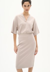 Beige, knielanges Kleid mit kurzen, lockeren Ärmeln, V-Ausschnitt und einem elastischen Taillenbund für eine figurbetonte Silhouette. Glatte Textur.