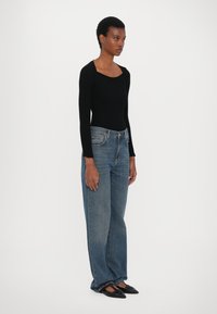 Svart ribbevest topp med lange ermer, høyt liv, blå vide jeans og spissede svarte leiligheter. Enkel, tettsittende design med en teksturert finish.