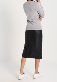 Grå stickad tröja, svart läder midi kjol och vita sneakers. Kläderna har en figurnära siluett och mjuka texturer.