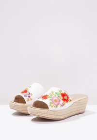 Sandales compensées blanches avec bout ouvert, décor floral brodé en rouge, rose et violet, avec une semelle en jute texturée.