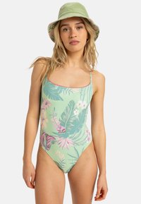 Einteiliger Badeanzug in hellem Mintgrün mit Blumen- und Blättermustern. Verfügt über dünne Träger und eine gewellte Kante. Kombiniert mit einem grünen Bucket Hat.