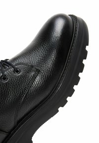 Zapato de cuero negro con un acabado texturizado, puntera redonda, diseño de cordones y una suela de goma gruesa y resistente con tacos pronunciados.