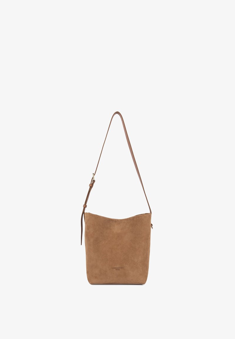 Sac à épaule en daim marron avec bandoulière réglable et marquage minimal sur le devant, présenté sur un fond blanc simple.