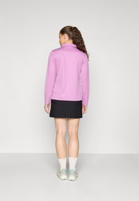 Lilla langermet topp med krage, kombinert med en mørk skjørt. Har en glatt tekstur og avslappet passform, brukt med lyse sneakers.