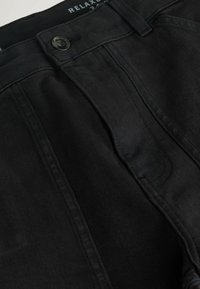 Black relaxed-fit trousers made of cotton fabric, featuring a button closure, flat front, and subtle stitching detail along the seams.