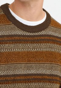 Brązowy sweter w wzory z okrągłym dekoltem. Posiada naprzemienne paski w różnych odcieniach brązu i kremu z teksturowymi wzorami.