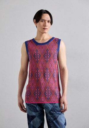 Mouwloze tanktop in felroze met blauwe accenten, met een diamanten patroon. G gedragen met blauwe gemusterde jeans, met een ontspannen pasvorm.