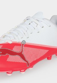 Λευκό και κόκκινο ποδοσφαιρικό παπούτσι Puma με λευκά κορδόνια και μαύρο λογότυπο Puma στο πλάι με διαμορφωμένες τάπες στη σόλα.