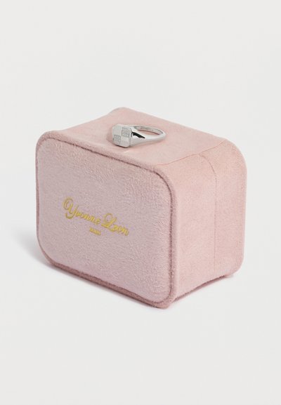 Růžová semišová krabička na prsten s zaoblenými hranami, zdobená zlatým nápisem "Yvonne Leon" a stříbrným prstenem se čtvercovými ozdobami nahoře.