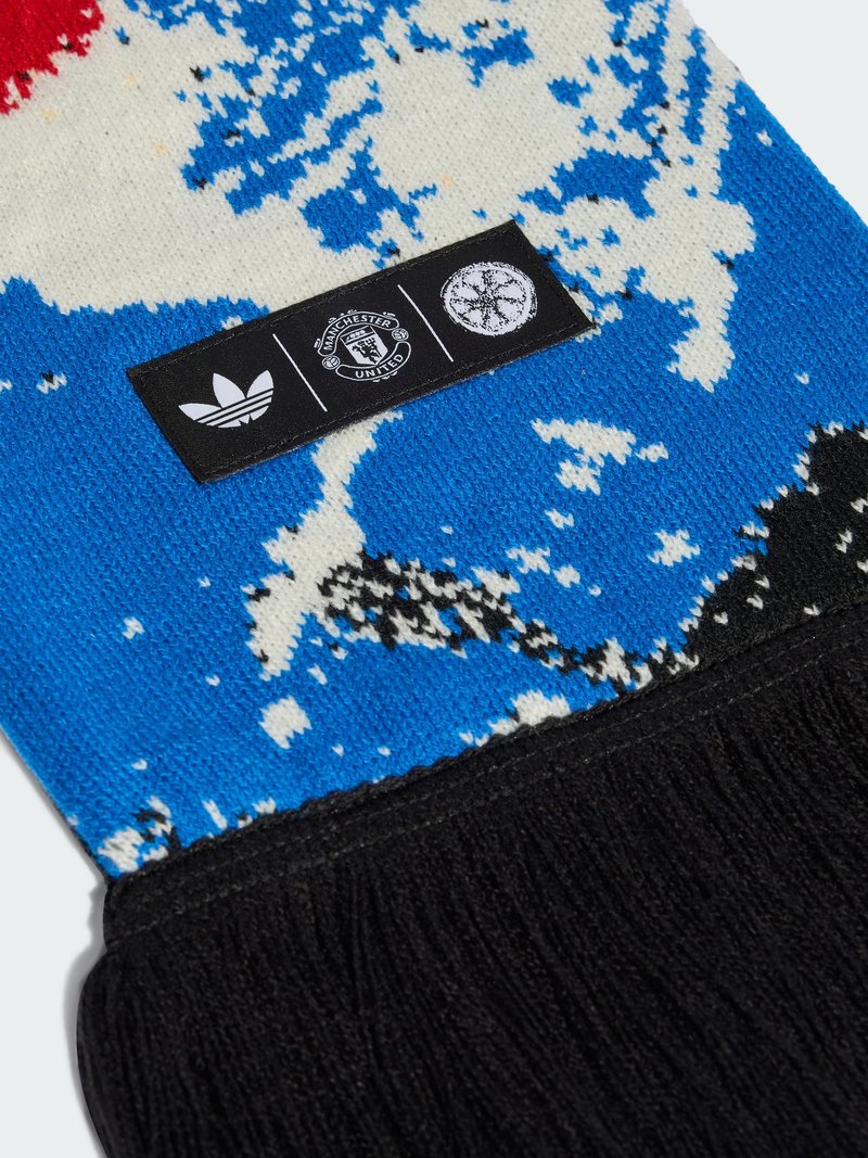 Sciarpa nera a maglia con motivi blu, bianchi e rossi, con i loghi Adidas, Manchester United e un albero circolare su un'etichetta nera.