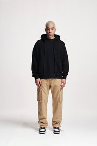 Zwarte zip-up hoodie met voorzakken, gecombineerd met beige cargo-broeken met zijzakken en zwart-witte sneakers.