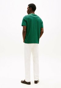 Grønstribet t-shirt i blødt materiale, korte ærmer, rund halsudskæring, parret med hvide bukser og mørke sko, set bagfra.