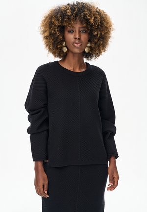 Czarny sweter o fakturowanej strukturze z okrągłym dekoltem, luźnymi rękawami i geometrycznym wzorem, w komplecie z pasującą czarną spódnicą.