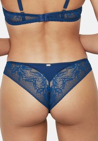 Navy blauwe kant string met bloempatronen en delicate gekartelde randen. Heeft een naadloos ontwerp voor comfort. De achterkant toont ingewikkelde details.