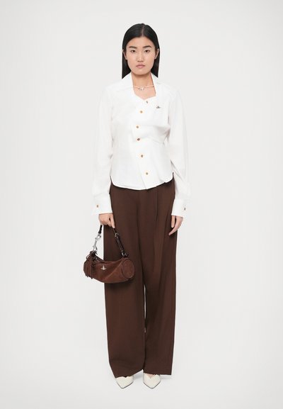 Fehér, gombos ing narancssárga gombokkal, barna, bőszárú nadrág, valamint egy barna, velúr kézitáska ezüst fém díszítéssel és bojttal.