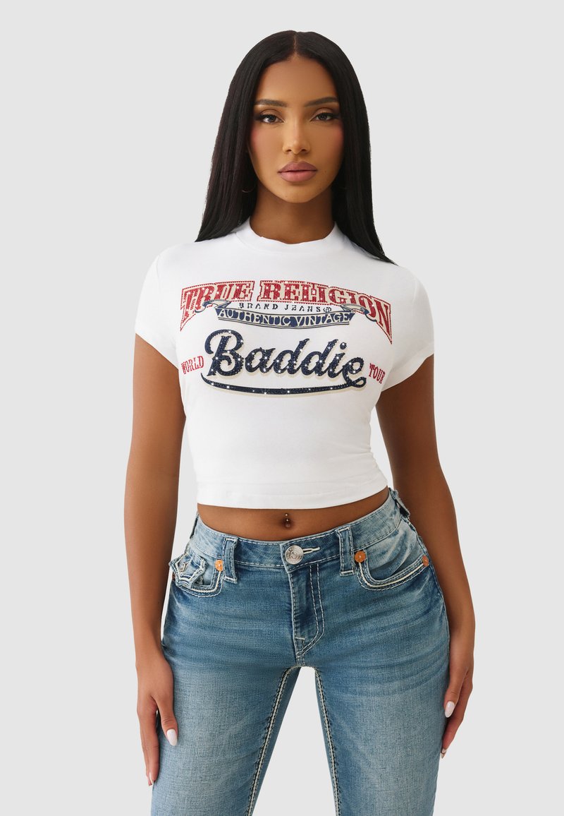 Biały krótki t-shirt z wielokolorowym nadrukiem tekstu "True Religion" oraz "Baddie", zestawiony z jasnoniebieskimi dżinsami z akcentującym przeszyciem.