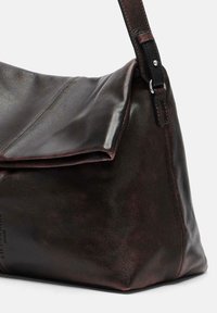 Sac à épaule en cuir marron foncé avec un rabat pliant et une bandoulière réglable, présenté sur un fond clair et uni.