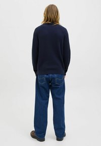 Navy ribbed knit sweater with a high neckline, paired with loose-fitting denim jeans featuring rear pockets and a slightly tapered leg.