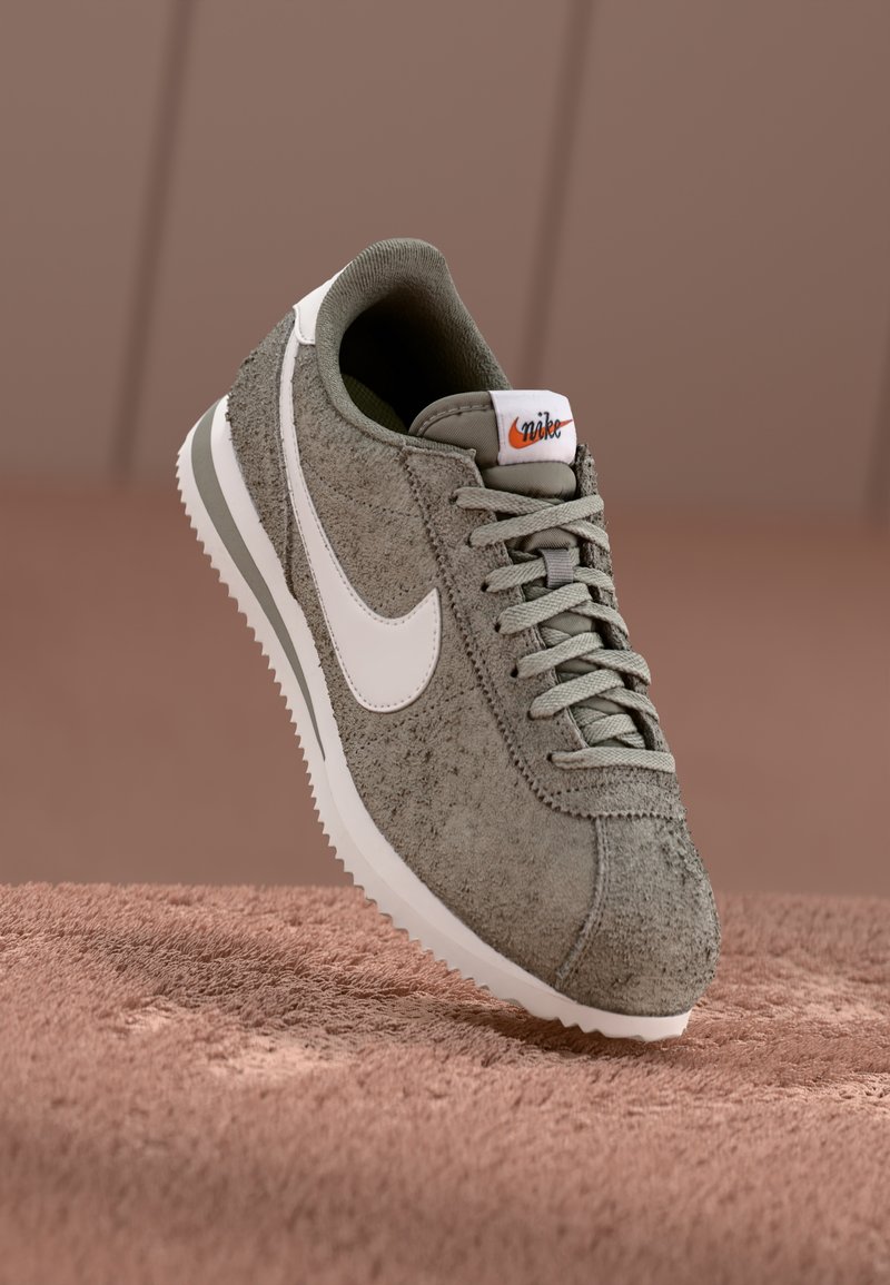 Nike tenisky v olivovo zelenej zamši s bielym logom Swoosh, textúrovaným zvrškom a svetlým gumovým podrážkou, s šedými šnúrkami a detailmi.