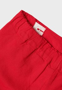 Pantaloni rossi in cotone con vita elasticizzata, dotati di un'etichetta bianca e dettaglio con bottone sul retro, texture liscia e design semplice.