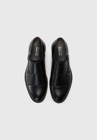 Black vegan leather shoes with a rounded toe, double buckle strap closure, and textured stitching along the sole. Smooth surface finish.