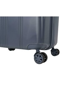 Maleta gris con superficie texturizada, rayas verticales y cuatro ruedas negras, dos de las cuales son dobles para una mayor movilidad.