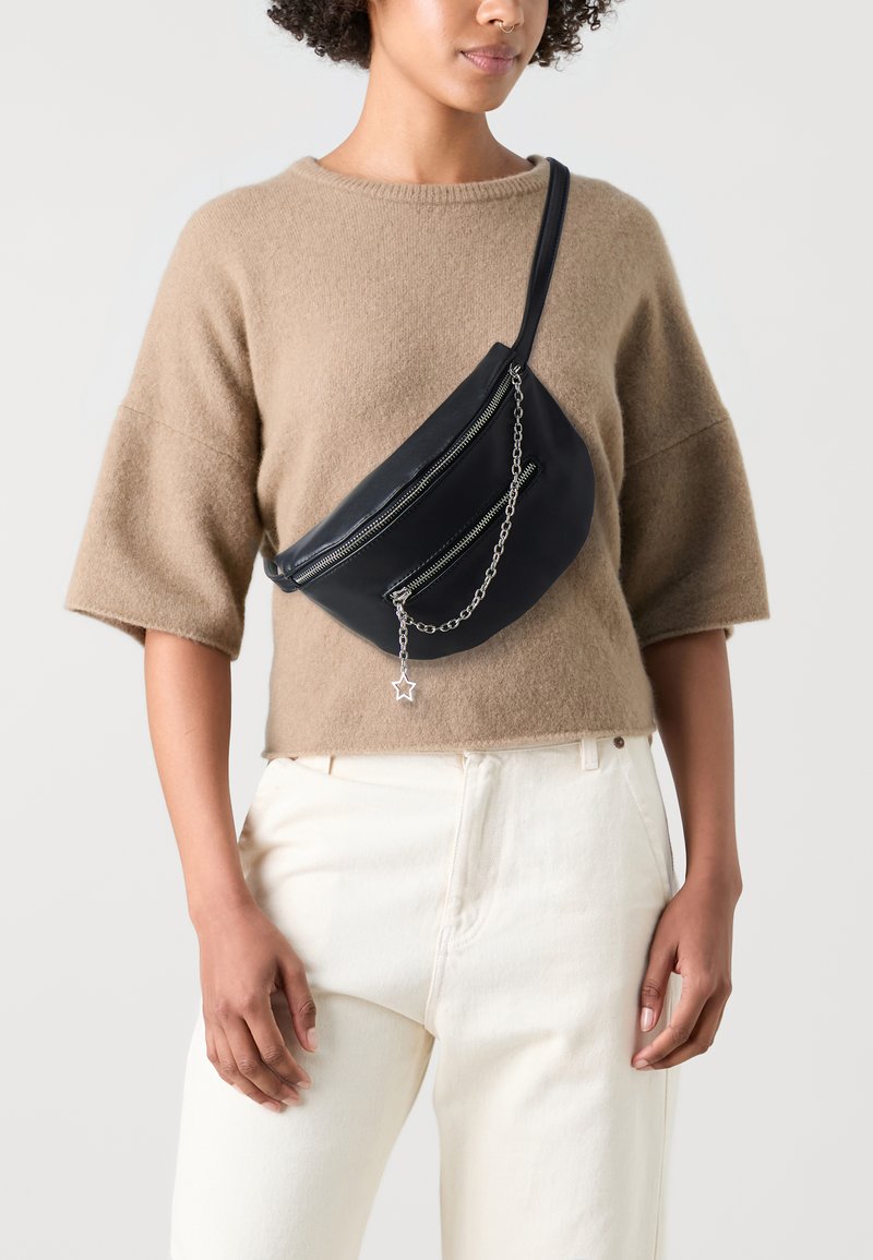 Borsa a tracolla in pelle nera con una forma curvata, due scomparti con zip, un accento in catena argento e un dettaglio a forma di stella.