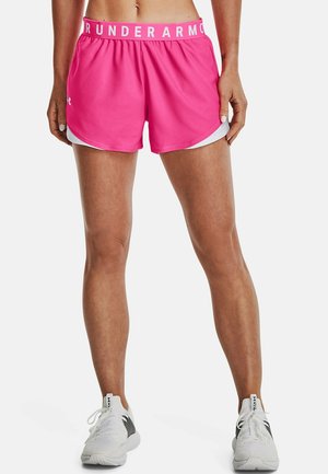 Femme portant un short de sport rose vif avec bordure blanche et taille élastique, assorti à des chaussures de sport blanches et noires sur fond gris.