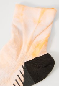 Flerfargede sokker med et design av fersken- og gulgradering, svart manchet, teksturert stoff og subtile horisontale striper på sålen.