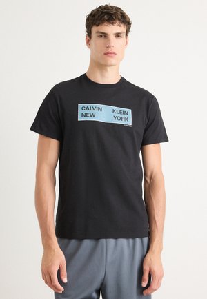 Crna pamučna majica s centriranim svjetloplavim grafičkim prikazom s tekstom "CALVIN KLEIN NEW YORK". Glatka tekstura i klasičan dizajn s Crew neck izrezom.