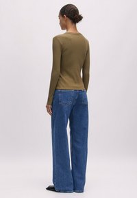 Olijfgroen geribbeld shirt met lange mouwen, gecombineerd met oversized blauwe spijkerbroek. Heeft een ronde hals en een ontspannen pasvorm. Effen textuur.