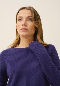 Lila gestrickter Pullover mit einem strukturierten Rippmuster, ausgestattet mit einem weiten Ausschnitt und langen Ärmeln. Weicher Stoff mit einer lässigen Passform.