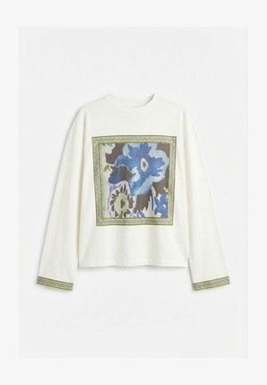 Balti ilgomis rankovėmis marškiniai su dideliu mėlynos gėlės kvadrato raštu priekyje ir atitinkamomis apvado detalėmis ant rankovių rankogalių.