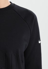 Černá mikina se žebrovanou strukturou, s kulatým výstřihem a raglánovými rukávy. Obsahuje malé bílé logo Nike na pravém rukávu.