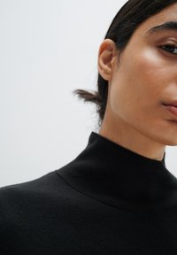 Pulover negru cu guler înalt, având o textură moale din tricot, design aderent, prezentat pe umărul și linia maxilarului unui model.