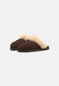 Brune semskede tøfler med en kremfarget faux fur-fôr langs den åpne toppen. Myk, avrundet tådesign og flate såler for komfort.
