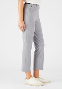 Grijze pinstripe broek met een recht model, voorzien van zijzakken en een getailleerde pasvorm. G gedragen met witte sneakers.