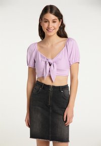 Ljubičasti crop top s napučenim rukavima i vezanjem sprijeda, uparen s visokim crnim traper suknjom s prednjim zatvaračem i poderanim rubom.