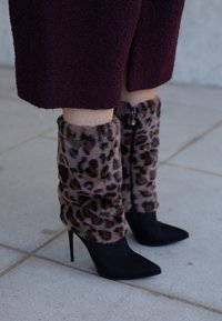 Nogawice z futra w panterkę z czarnym zamszowym obcasem w szpic, z zamkiem błyskawicznym i trójkątnym metalowym akcentem.