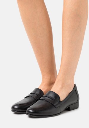 Mocassins en cuir noir à talon bas, présentant un design épuré, une texture lisse et des détails cousus sur le dessus.