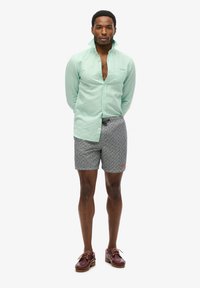 Muntgroene lange mouwen shirt, ongebotonneerde kraag, grijs gemarmerde shorts en bordeauxrode schoenen met bruine zolen. Eenvoudige, casual outfit.