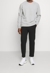 Sweat-shirt gris en polaire avec col rond, pantalon noir fuselé, et baskets blanches. Comprend des poignets et un ourlet côtelés, avec les revers du pantalon retroussés.