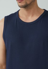 Marineblauwe mouwloze tanktop van ribstof, met een ronde halslijn en textuurdetails langs de armsgaten en de zoom.