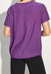 Top viola a maniche corte con una vestibilità rilassata, caratterizzato da una texture a costine e dettagli con orlo arrotolato, abbinato a pantaloni neri.