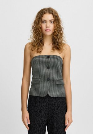 Top bustier noir et blanc en motif pied-de-poule avec trois boutons, coupe cintrée et deux poches devant. Porté avec un pantalon noir texturé.