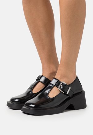 Chaussures Mary Jane en cuir verni noir avec une bride à boucle, un design T-bar, un talon épais et un bout arrondi. Texture lisse et finition brillante.