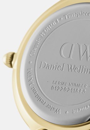 Zlato obarvana hrbtiščna strani ura s srebrnimi detajli. Vgravirano besedilo vključuje ime blagovne znamke "Daniel Wellington" in serijsko številko, skupaj s podrobnostmi o vodoodpornosti.
