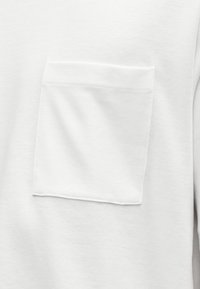 Λευκό βαμβακερό t-shirt με μία τσέπη στο στήθος. Το ύφασμα έχει λεία υφή με απλό, καθαρό σχέδιο.