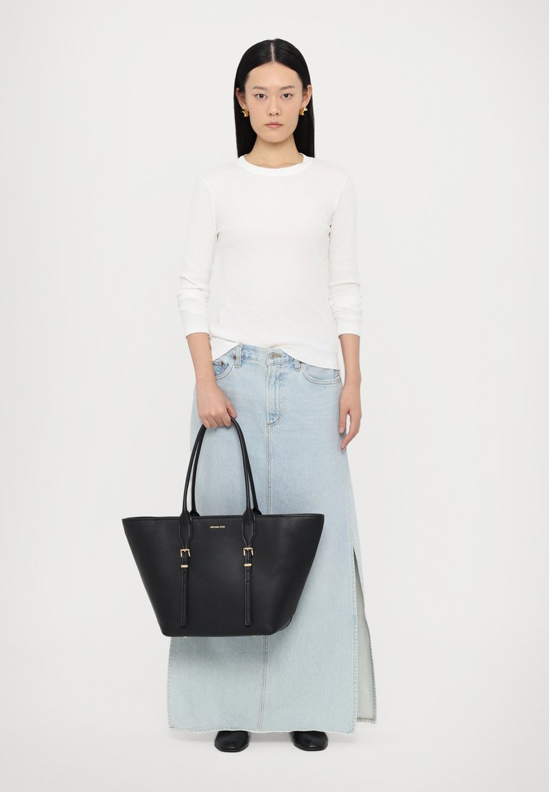 Sac en cuir noir avec un large fond et un sommet rétréci, doté de quincaillerie dorée, de poignées doubles et d'une texture lisse.