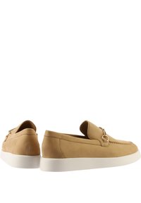 Tanfarbene Slip-On-Schuhe mit runder Zehenform, kontrastierender weißer Gummisohle und einem dekorativen Metallring an der Seite. Glatte Textur.